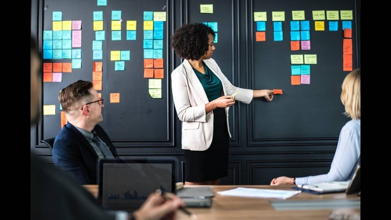 Woman presenting in front of a blackboard with colorful sticky notes.
