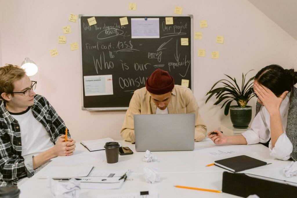 Team working around a laptop with notes and a chalkboard in the background.