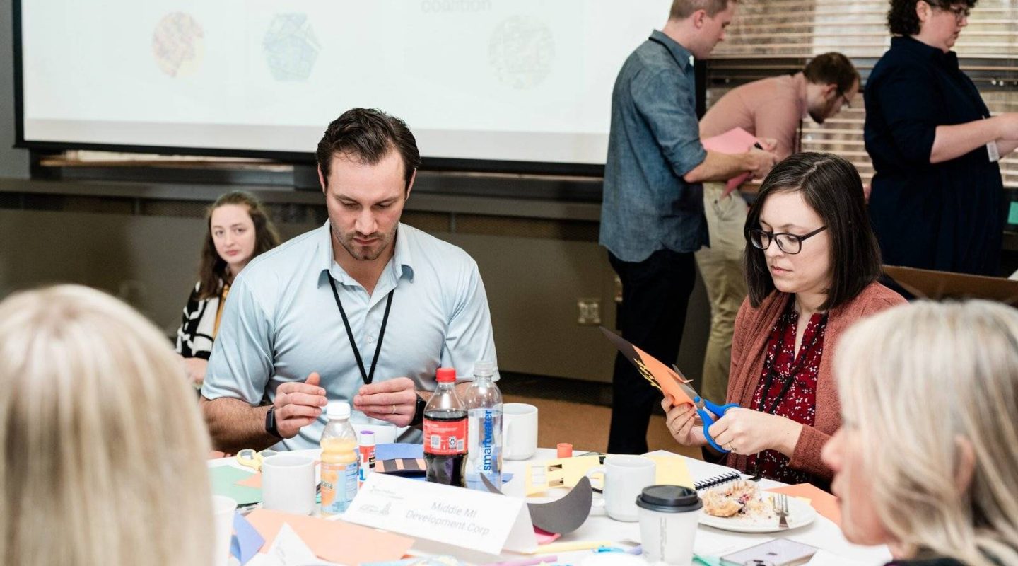 People sitting around a table in a workshop or conference setting, engaged in a discussion or activity.
